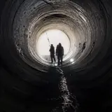 Silhouettes of two workers inside a massive water pipe at a construction site for irrigation infrastructure